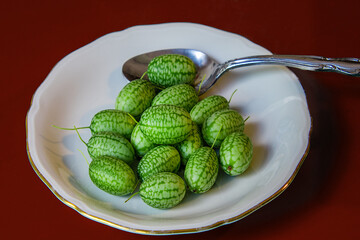 Fresh green cucamelon fruits in a dish with a spoon on a red table