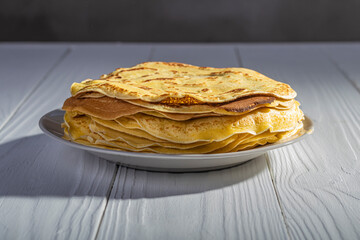 white wooden background in retro style. the plate in it is thin yellow pancakes. close-up.