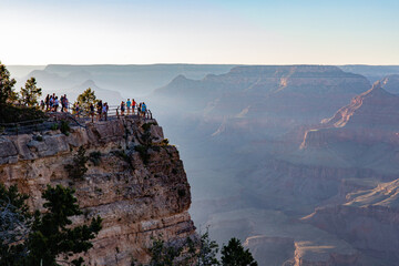 Grand Canyon in Arizona overlook with sunlight casting across the horizon at the national park with people.