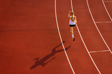young woman in sports uniform runs along the track of the stadium, back view. sports training and...