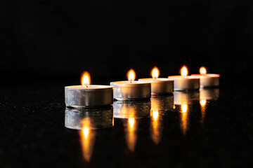 Five candles in a row on black reflected surface
