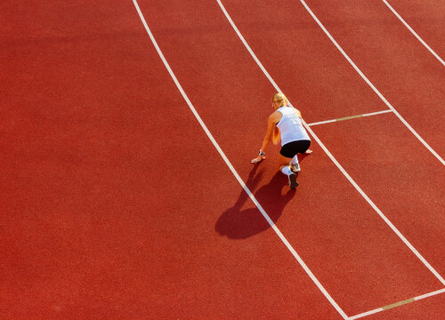 young woman in sports uniform crouched for a low start at the running stadium, back view. sports training and exercise. healthy lifestyle