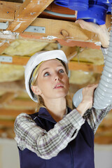 female elctrician fitting air conditions pipe in building ceiling