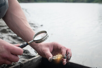 Treasure hunter is picking a golden ore from dirty metal grid on the river water background....