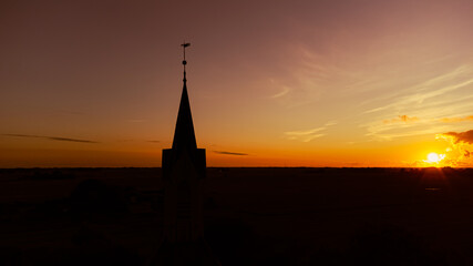 Obraz premium Kirche und Kirchturm im Sonnenuntergang mit weiter Landschaft und Natur im Hintergrund