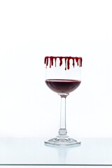 Bloody Halloween drink with red dripping decoration of the wine glass in front of white background and space for copy text