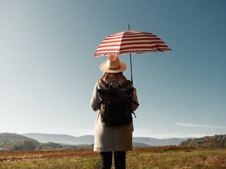 woman in coat with backpack and umbrella on mountain background