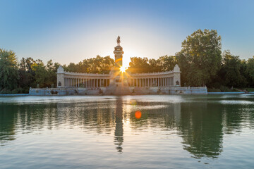 Sunbeams coming behind a statue of 1902 during a sunrise at the lake of the Retiro Park of Madrid. A popular place for leisure activities such as walking or renting a boat for rowing. - obrazy, fototapety, plakaty