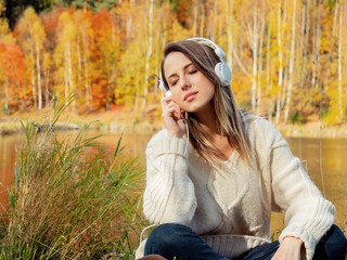 woman with headphones near lake in autumn time