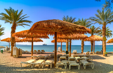 Morning on sandy beach of the Red Sea in Eilat - famous tourist resort city in Israel, at the distance seen ocean cargo ship going to the marine port of Eilat