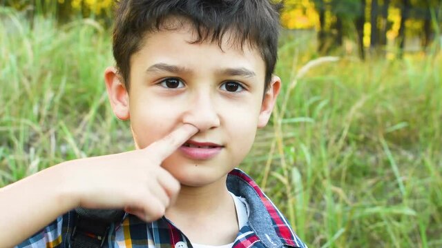 the boy picks his nose with his finger