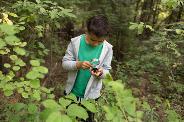 young boy exploring nature in the forest with magnifying glass