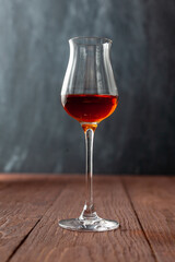 Grappa glass with brandy or sherry or calvados on wooden table.