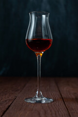 Grappa glass with brandy or sherry or calvados on wooden table in dark mood.