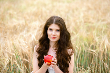 Portrait of pretty woman in summer outfit holding ripe apple in field, horizontal image