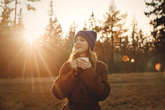 Young woman with cup of coffee stay near wood in sunset time