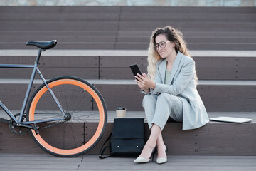 Fototapeta na wymiar Happy businesswoman looking at smartphone screen while having break in urban environment