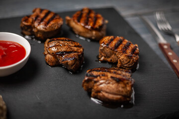 Grilled pork medallions with ketchup on dark wooden table. Folk and knife. Close up.