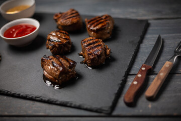 Grilled pork medallions with ketchup and mustard on dark wooden table. Folk and knife.