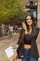 Nice Caucasian girl with bags in her hand looks at you and smiles as she moves around. Vertical version