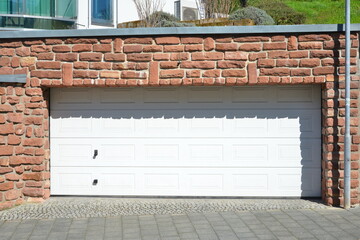 Garage mit elektrischem Automatik-Rolltor und roter Natur-Sandsteinmauer und Edelstahl-Attika zum...