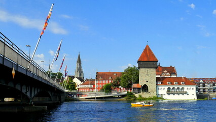 malerischer Blick auf alten Rheintorturm in Konstanz mit Brücke und bunten Häusern unter blauem...