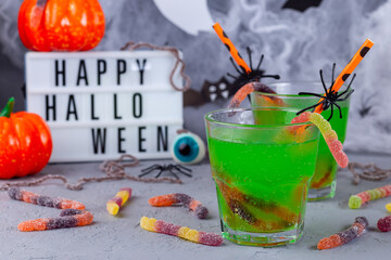 Spooky Halloween cocktail with green bubble drink and candy worms, light box on background