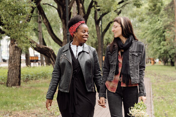 Happy intercultural girlfriends looking at one another while moving along park