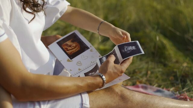 Husband and wife are expecting baby resting in nature and examining an ultrasound image of woman's uterus in which fetus is growing. Dad strokes picture of a baby. Parental love for the unborn child.