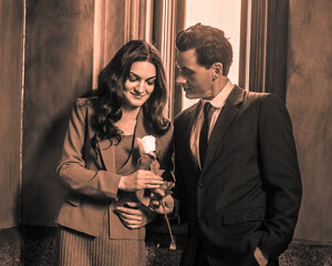 A young handsome businessman is giving a white flower to a pretty businesswoman after work..