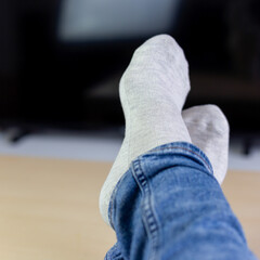 Relaxing woman laying in sofa front of TV, holding her legs on table