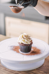 The girl sprinkles cocoa on the cupcakes through a sieve