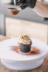 The girl sprinkles cocoa on the cupcakes through a sieve