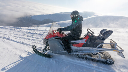 The snowmobile moves on the slope of a snow-capped mountain.