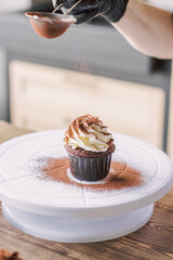 The girl sprinkles cocoa on the cupcakes through a sieve