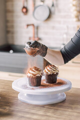 The girl sprinkles cocoa on the cupcakes through a sieve