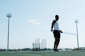 A purposeful African-American male track and field athlete in a white T-shirt jumps on a rope
