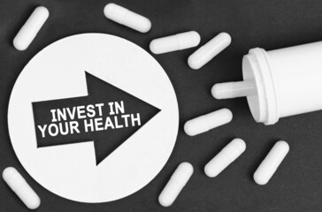 Pills on a black background. A circle with an arrow, inside it is written - INVEST IN YOUR HEALTH
