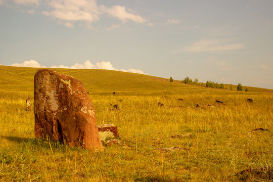Burial mound in the endless steppe in republic of Khakassia, Russia. Ancient stone menhir in the steppe. Summer evening landscape in warm tones