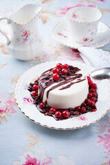 Traditional blancmange almond pudding with currant berries, chocolate cream and crumples served as close-up in a classic design plate