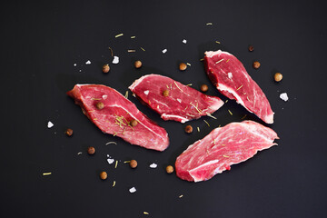 Slices of fresh raw beef steak with spices on black background. Top view flat lay with copy space