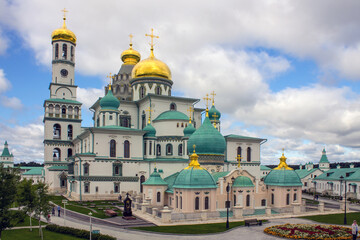 beautiful architectural ensemble of white stone churches with golden domes in New Jerusalem on a sunny summer day against a bright blue sky with clouds in Istra Moscow region Russia