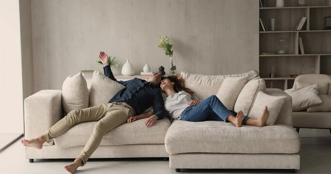 Overjoyed happy sincere young couple homeowners or renters jumping on big comfortable sofa, enjoying moving into new contemporary apartments, real estate service, bank mortgage loan, tenancy concept.