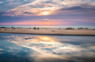 Colorful sunset over the Baltic sea from the pine forest viewpoint. Cloud reflections in calm water.