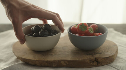 man put fresh strawberries and blueberries in bowls on olive wood board