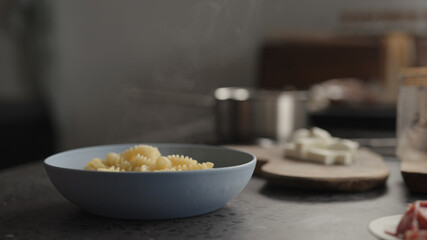 steam rising from boiled fusilli in blue bowl on concrete countertop