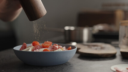 grinding black pepper over fusilli pasta in blue bowl
