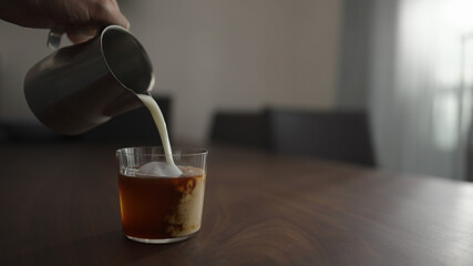 pour milk into cold brew coffee over ice ball in tumbler glass on walnut table