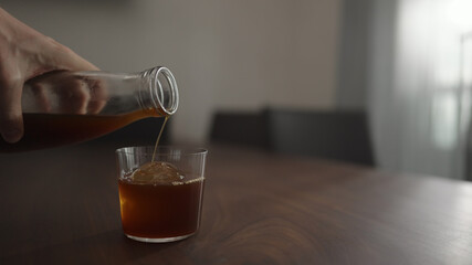 pour cold brew coffee over ice ball in tumbler glass on walnut table