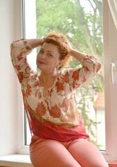 Beautiful woman sits on the windowsill and straightens her hair with her hands